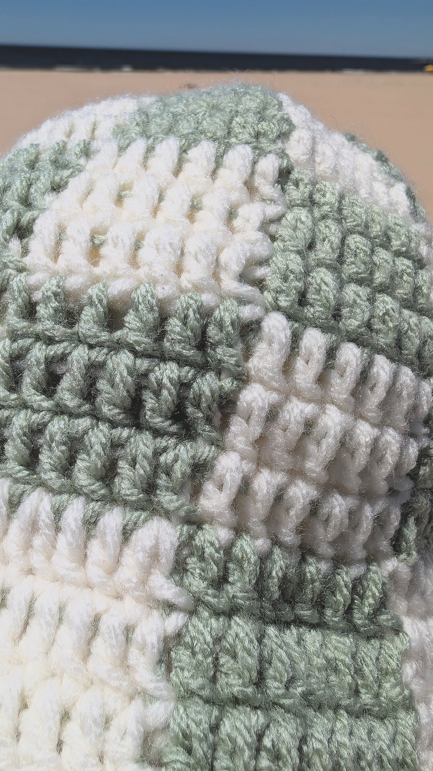 Close-up of a crocheted item with green and white pattern on a blurred background