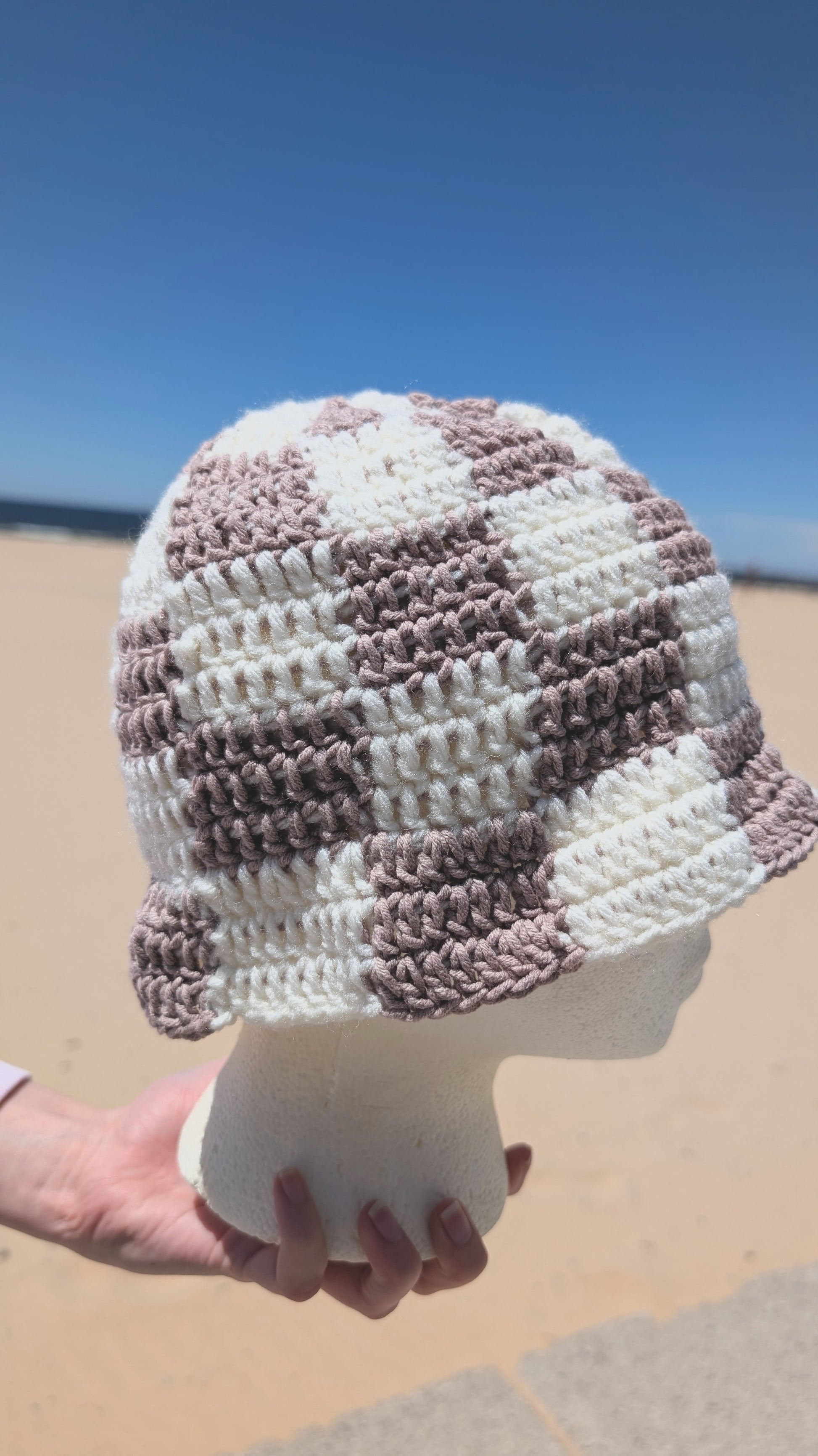 Checkered hat held by a hand on a beach with clear blue sky