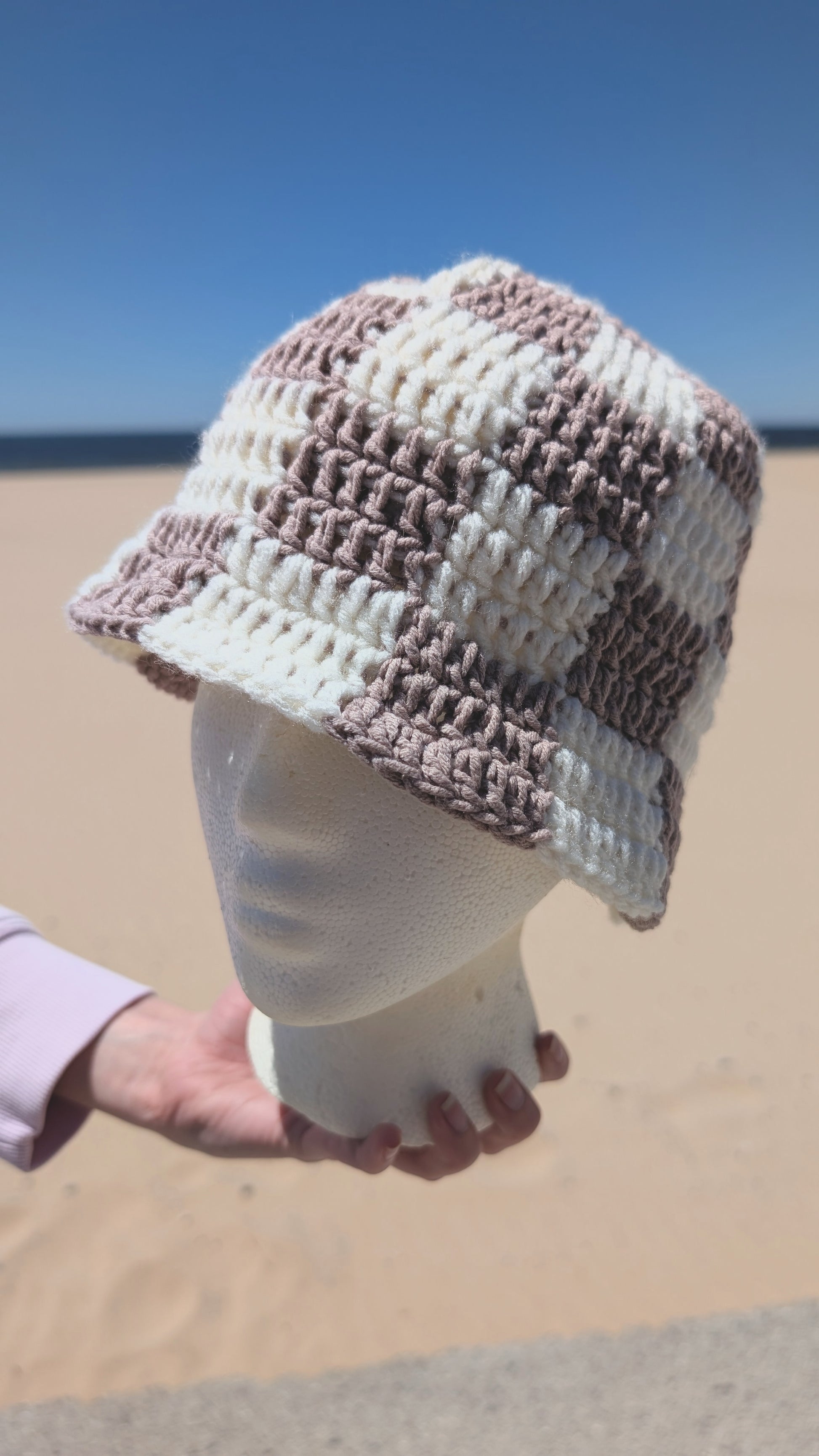 Crocheted hat on a mannequin head against a beach background