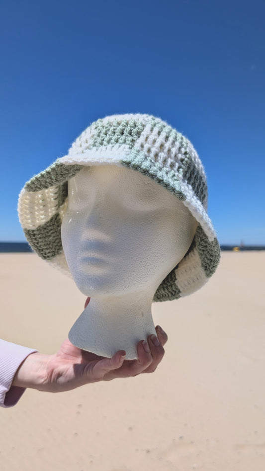 Mannequin head wearing a checkerboard hat on a beach with clear blue sky