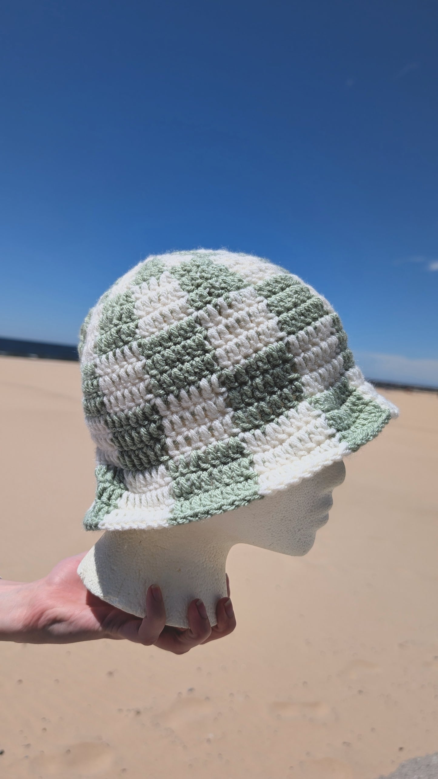 Handmade crochet hat on a mannequin head against a beach background