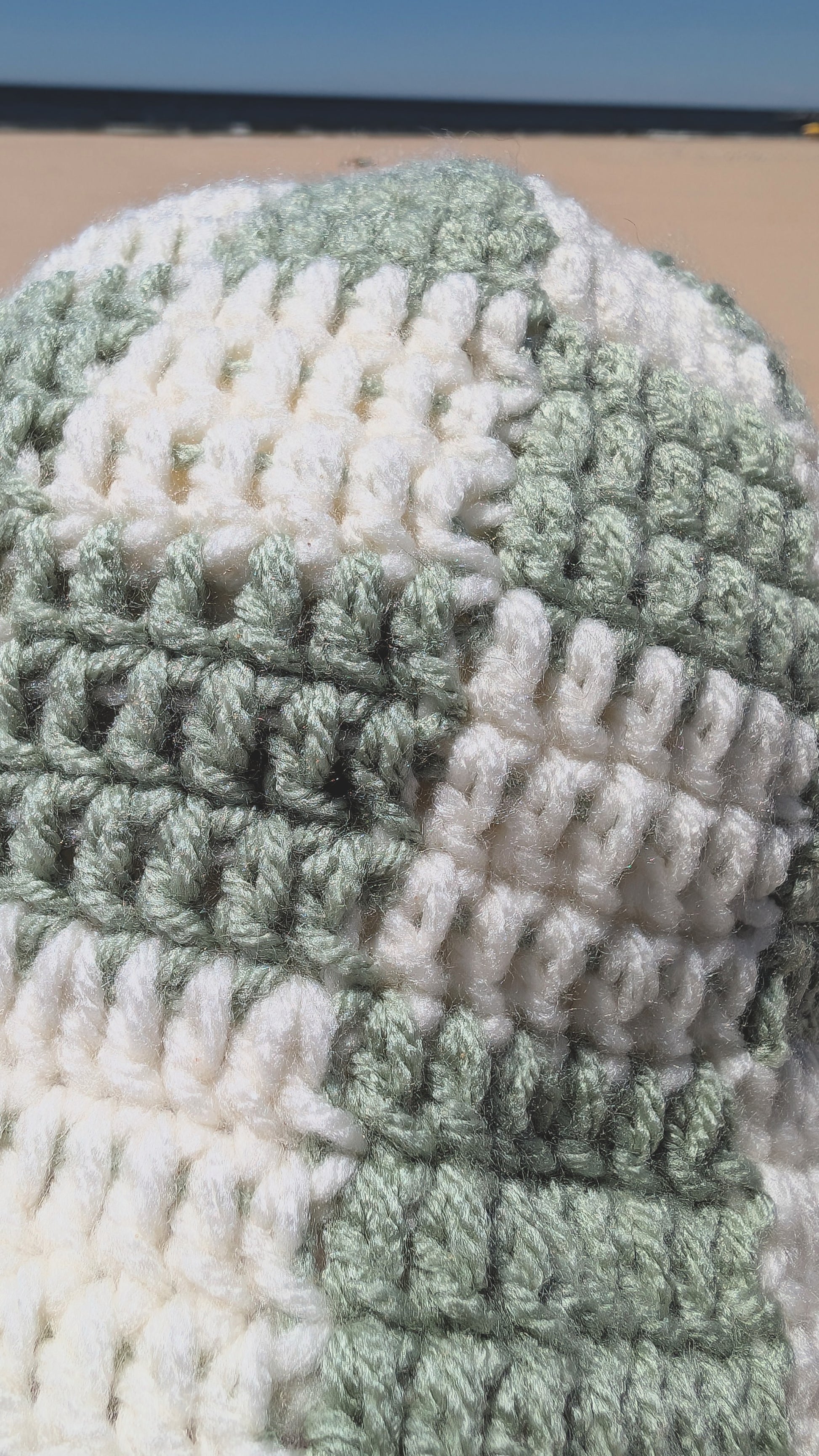 Close-up of a crocheted item with green and white pattern on a blurred background