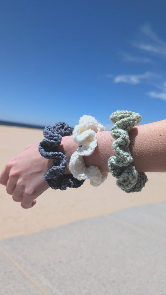 Three crochet scrunchies on a wrist with a clear blue sky in the background
